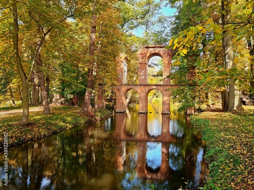 ceglany akwedukt odbijający się w rzece wśród drzew w parku