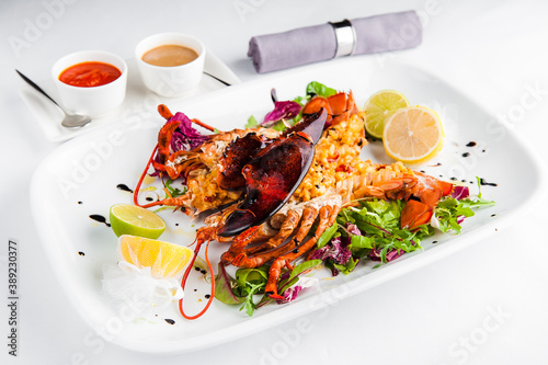 Lobster on a white plate with lemon, salad, lime and sauce