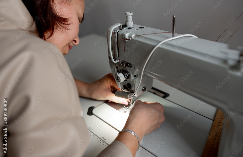 woman tailor puts thread in a needle in a sewing machine