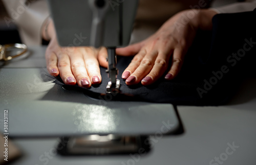 Close-up female hands sew a dark fabric on a sewing machine. Design studio, tailoring process concept. © александр таланцев