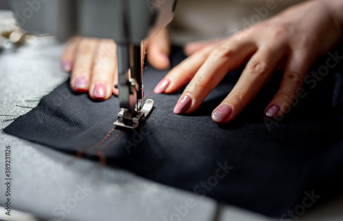 Close-up female hands sew a dark fabric on a sewing machine. Design studio, tailoring process concept.
