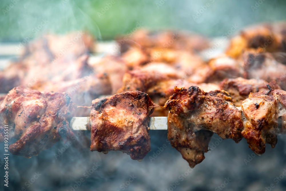 Shashlik or shish kebab preparing on barbecue grill over hot charcoal. Grilled pieces of pork meat on metal skewers.