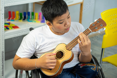 disability kid playing music with guitar on wheelchair with Autism child playing in special classroom