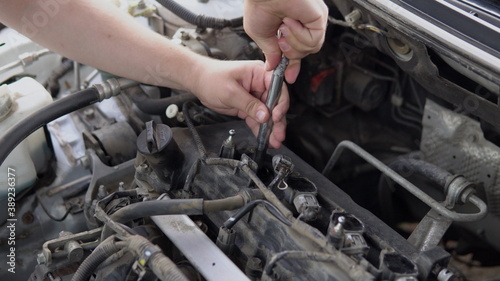 A man pulls out an old spark plug from a car engine