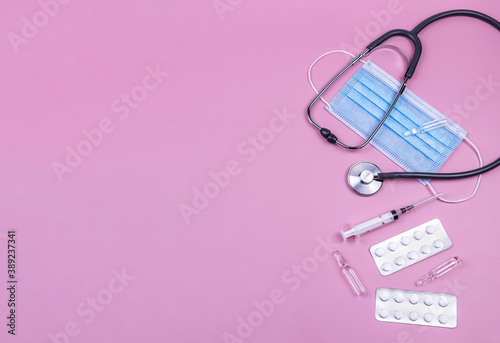 stethoscope, face mask, pills, syringe, ampoules, on a pink background.