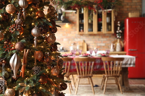 New year's holiday interior. Home environment. Large Christmas tree with decor and kitchen in the background in defocus