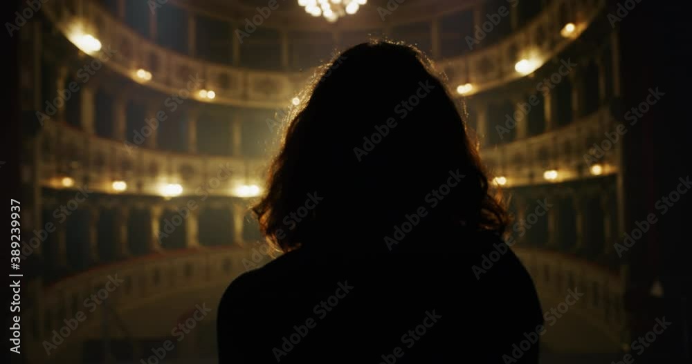 Cinematic back view shot of female artist or actress is going out on classic theatre stage with dramatic lighting for performance preview before start of show.