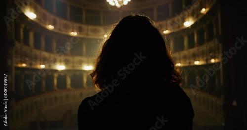 Cinematic back view shot of female artist or actress is going out on classic theatre stage with dramatic lighting for performance preview before start of show.