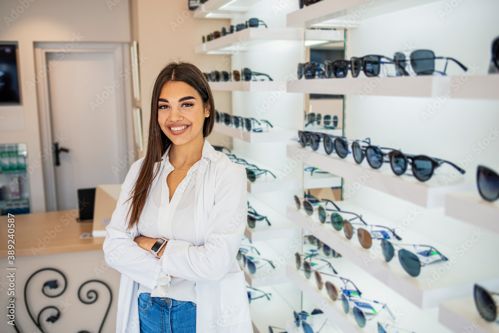 Optician selling glasses at the optics. Happy optician selling glasses and looking at the camera smiling. Friendly eye doctor selling glasses at an optician's shop and looking at the camera smiling