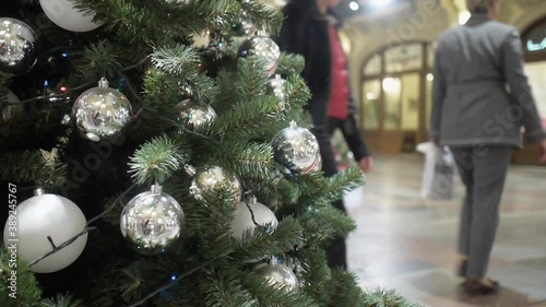 Looped video of visitors walking behind a Christmas tree decorated with silver balls in GUM