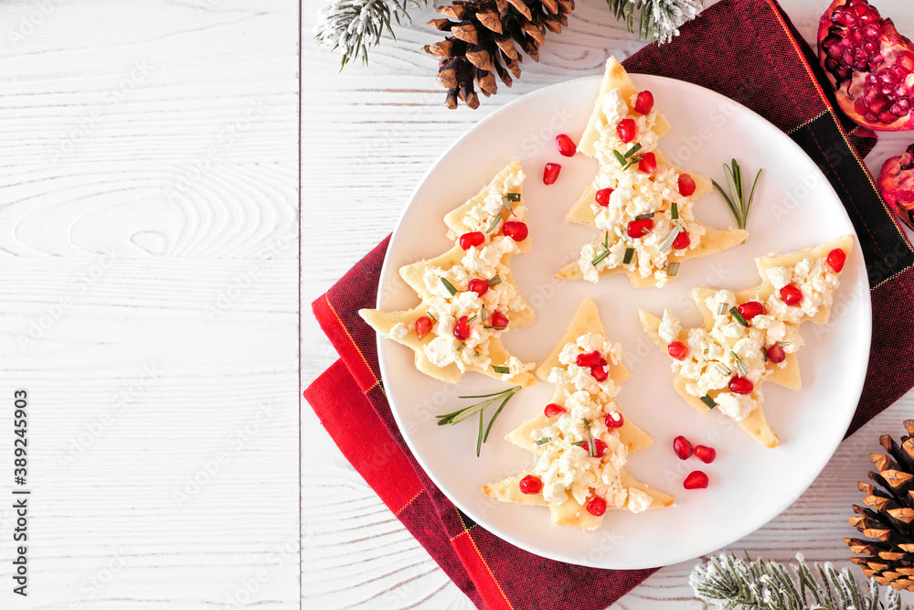 Christmas tree shaped appetizers with feta cheese and pomegranates. Table scene over a white wood background. Copy space.