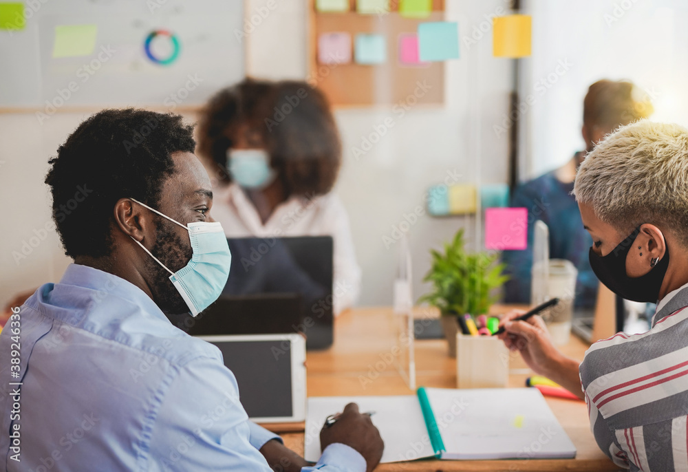 Obraz premium Young multiracial people at work in office while wearing protective face mask for coronavirus - Work places with new safety measures