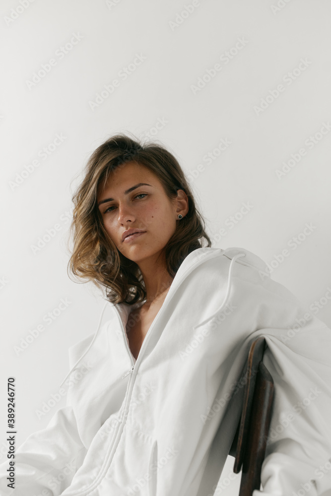 Portrait of beautiful young woman with brown hair and clean bronze skin without makeup on white background. Natural and healthy look. Neutral interior. Soft light. Portrait of beautiful young woman with brown hair and clean bronze skin without makeup on white background. Natural and healthy look. Neutral interior. Soft light.