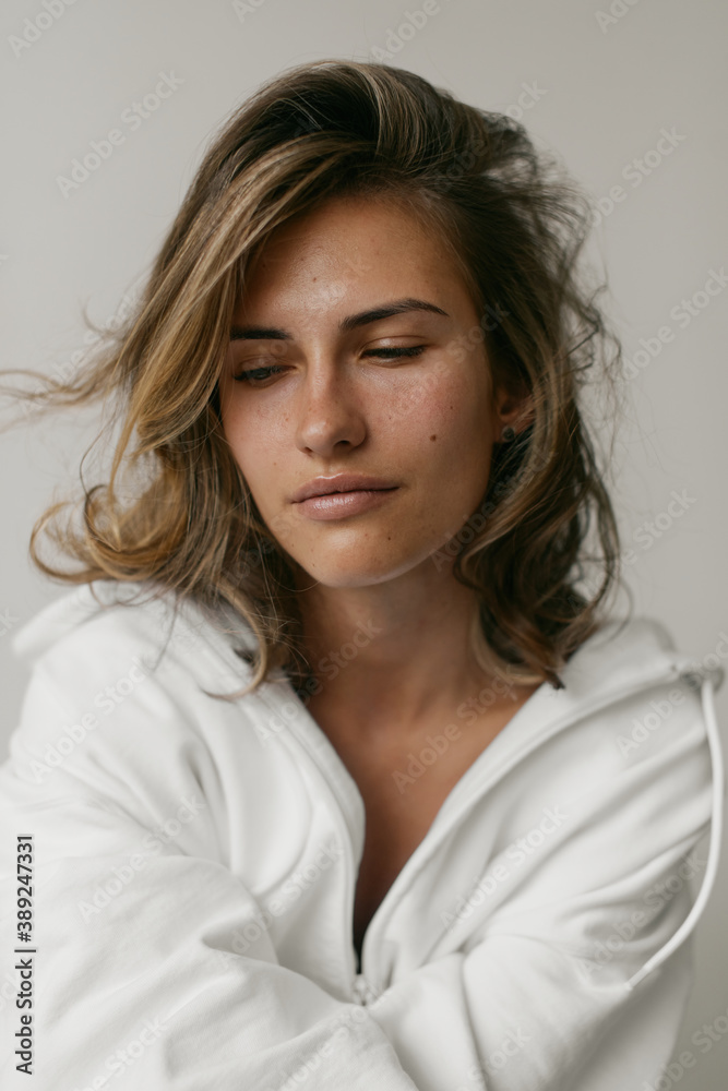 Portrait of beautiful young woman with brown hair and clean bronze skin without makeup on white background. Natural and healthy look. Neutral interior. Soft light. Portrait of beautiful young woman with brown hair and clean bronze skin without makeup on white background. Natural and healthy look. Neutral interior. Soft light.