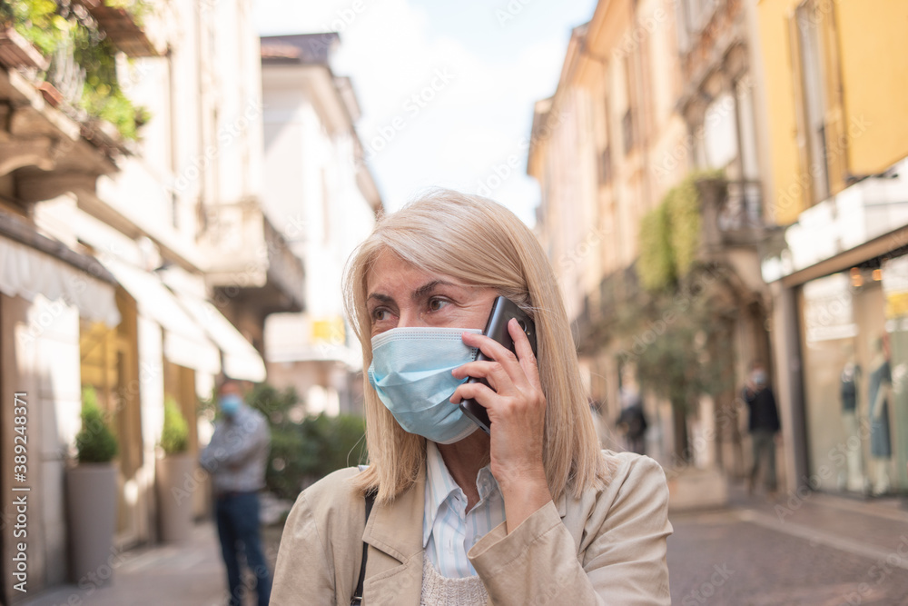 Masked woman talking on the phone while walking in a city street