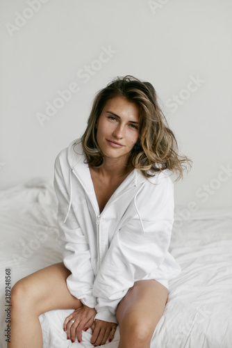 Portrait of beautiful young woman with brown hair and clean bronze skin without makeup on white background. Natural and healthy look. Neutral interior. Soft light. 