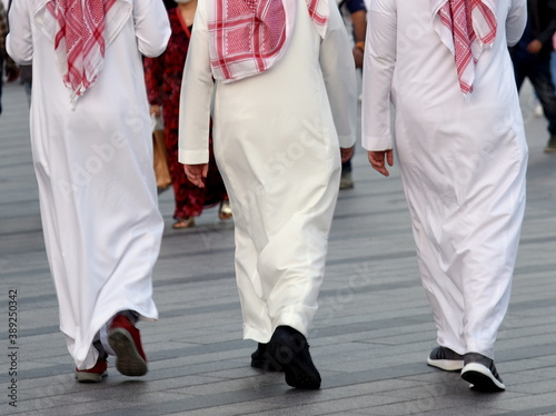 Drei traditionell bekleidete Emiratis mit langen weißen Gewändern und rotem Kopftuch