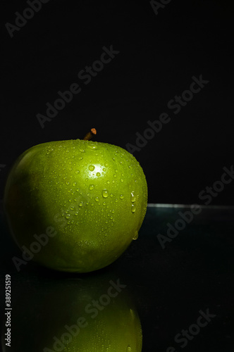 Close-up of fresh wet green apple on black background with reflection