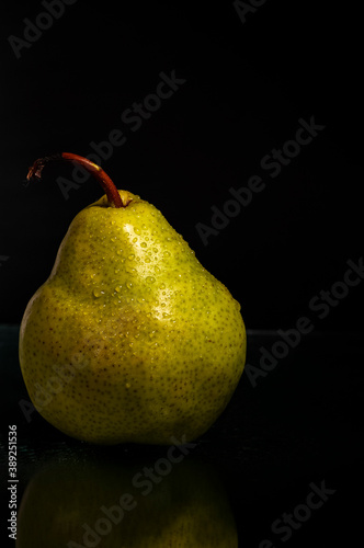 Close-up of fresh wet green pear on black background with reflection