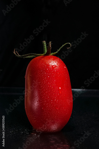a red, fresh, ripe, juicy tomato with green leaves and drops of water on dark background with copy space for text