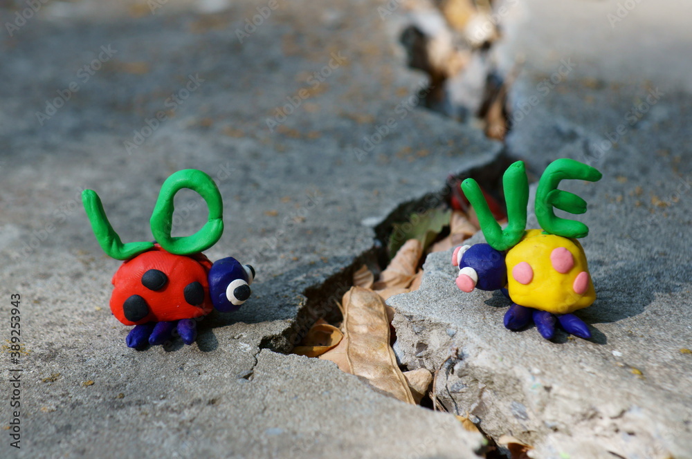 Figurines of two ladybirds made of plasticine. The figures are placed opposite each other. There's a crack between them. Next to it is the inscription love.
