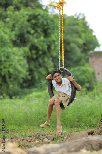 Cute indian child playing with swing made by tyre and rope on tree at green field © PRASANNAPIX