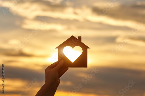 Woman hand holds wooden house in the form of heart against the sun photo