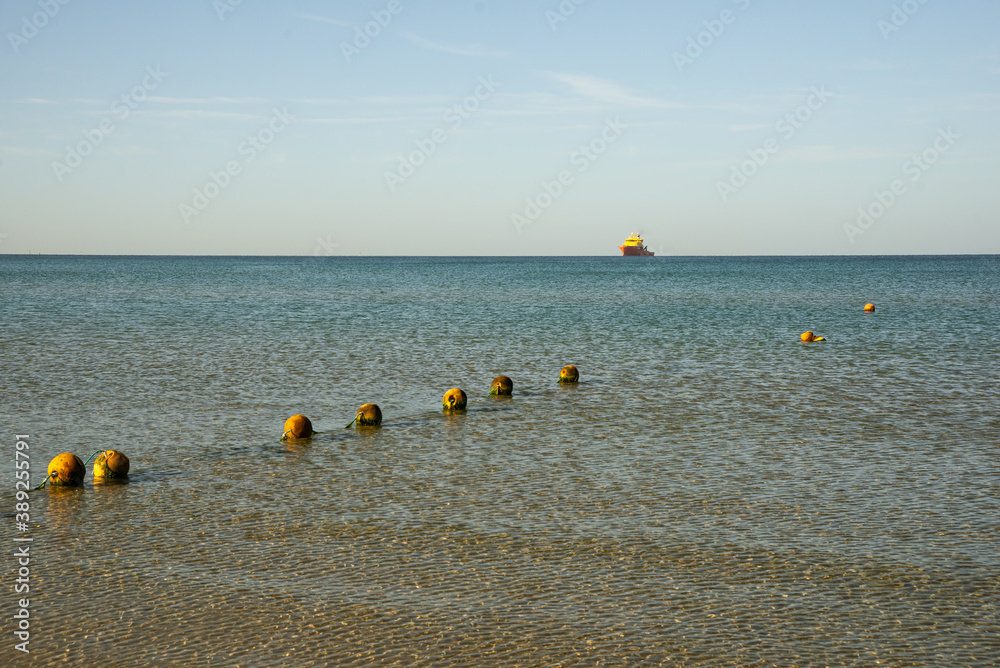 Endless sea, sunny morning, round old buoys in shallow water and a large cargo ship on the horizon