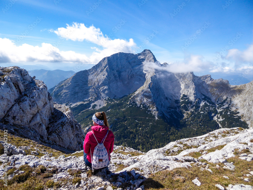 A woman in pink jacket enjoying the Alpine landscape from Hochzin?dl peak in Austria. Steep, sharp mountains around her. Fall landscape - golden grass. Exploring and experiencing the nature