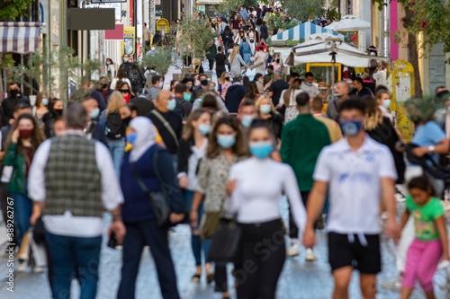 crowd goes up and down a busy shopping street wearing a protective mask