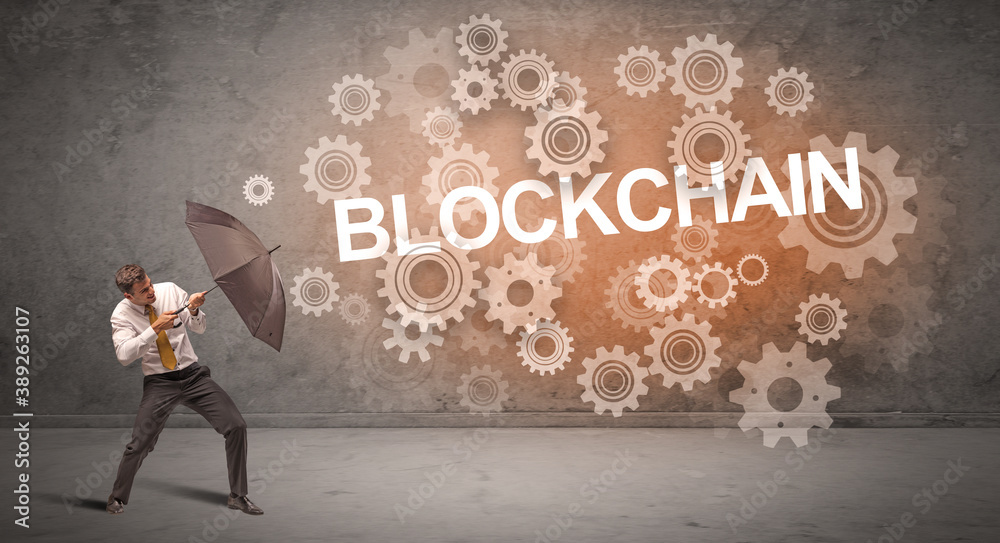 Businessman defending with umbrella from BLOCKCHAIN inscription, technology concept Businessman defending with umbrella from BLOCKCHAIN inscription, technology concept