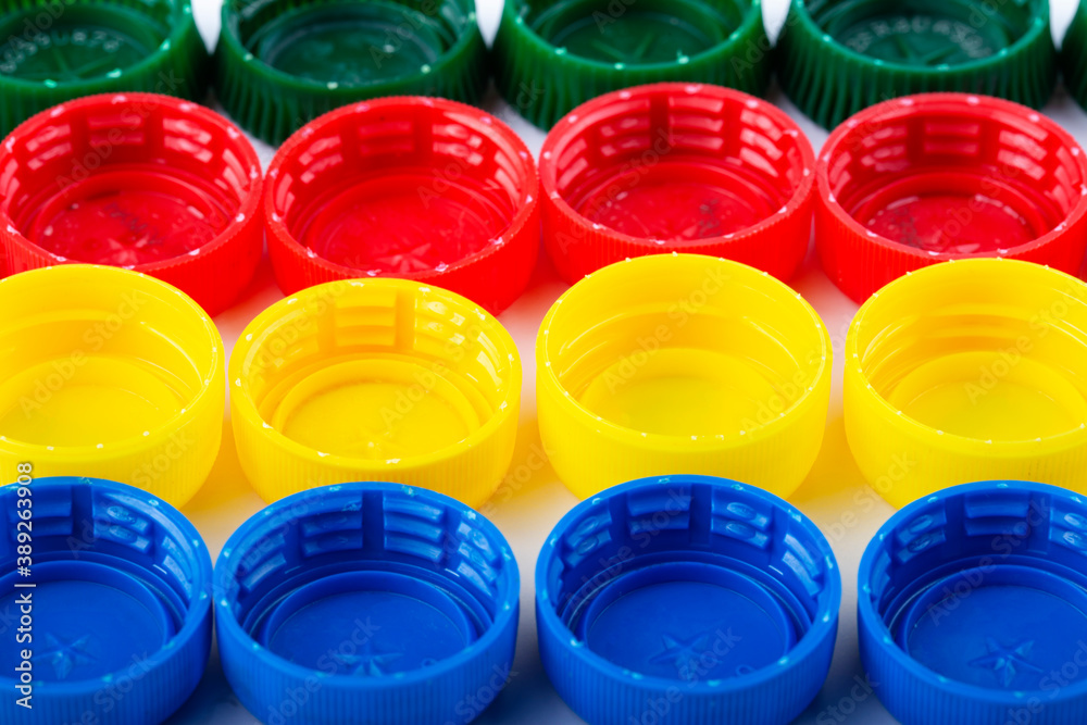 Plastic multi-colored bottle caps are arranged in rows on a white background. Plastic multi-colored bottle caps are arranged in rows on a white background.