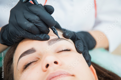 Young woman on permanent make-up procedure  tattooing eyebrows in natural tint. Eyebrow Correction closeup. Beauty Concept.