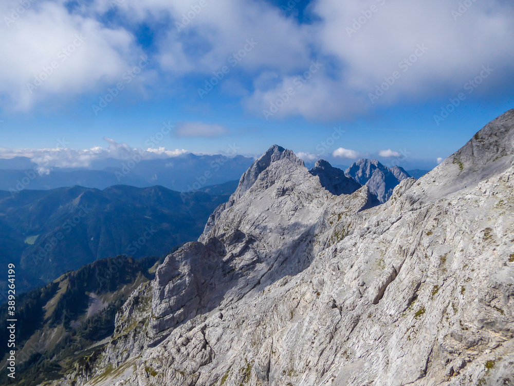 A panoramic view on endless mountain chains from top of a mountain in Hochtor region, Austrian Alps. High Alpine mountaineering. Sunny, cloudless summer day. Sharp and stony slopes in the foreground.