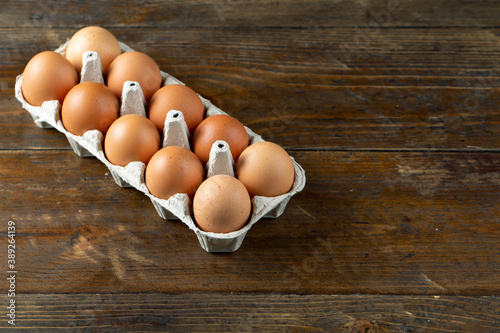 Chicken eggs in an open egg carton on wood background. Top view with copy space.