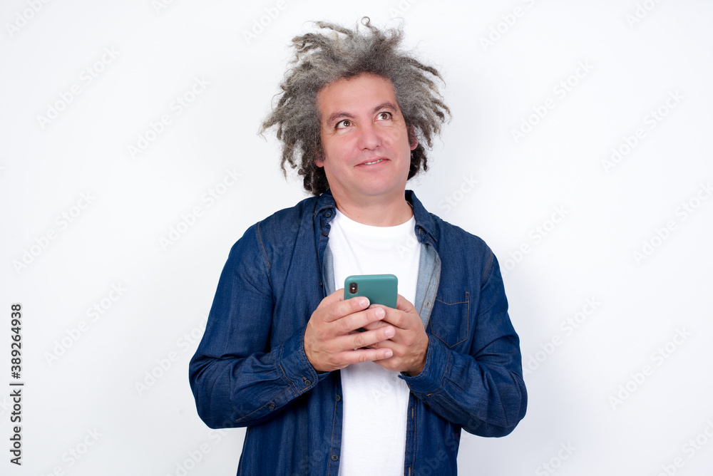 Image of a happy Handsome mature caucasian man with afro gray hair standing over white background listening to music with earphones using mobile phone. Image of a happy Handsome mature caucasian man with afro gray hair standing over white background listening to music with earphones using mobile phone.