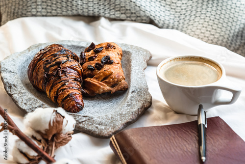 Coffee mug with croissant and empty notebook and pencil for business plan and design ideas onon white cloth from above, cozy and tasty breakfast, vintage toned photo