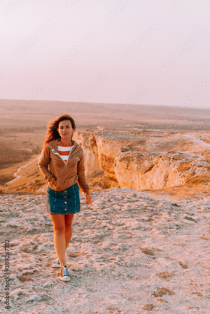 Rear view of a woman holding her long hair and walking on a rocky mountain in an orange sunset, the concept of tourism and freedom