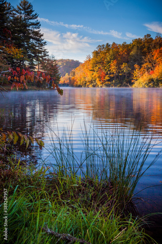 Autumn colors surround calm lake with mist in fall