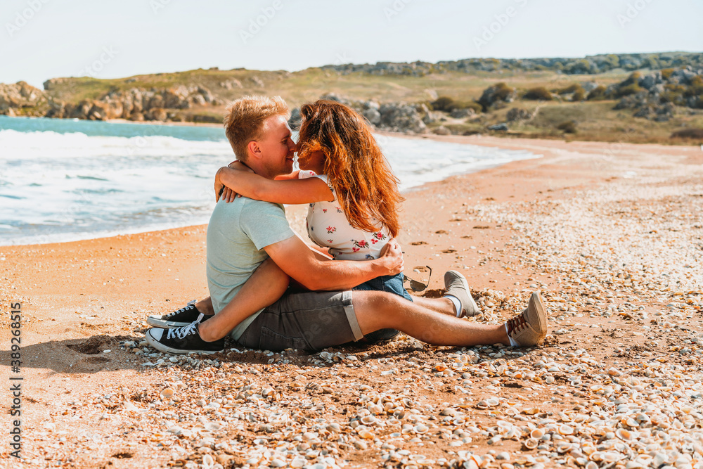 Happy romantic couple woman and man sitting on the beach near the sea and hug each other Happy romantic couple woman and man sitting on the beach near the sea and hug each other