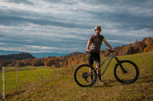Fototapeta Naklejka Na Ścianę i Meble -  Young caucasian mountain biker resting and posing on sunny meadow in autunn setting. Visible mountains in the background.