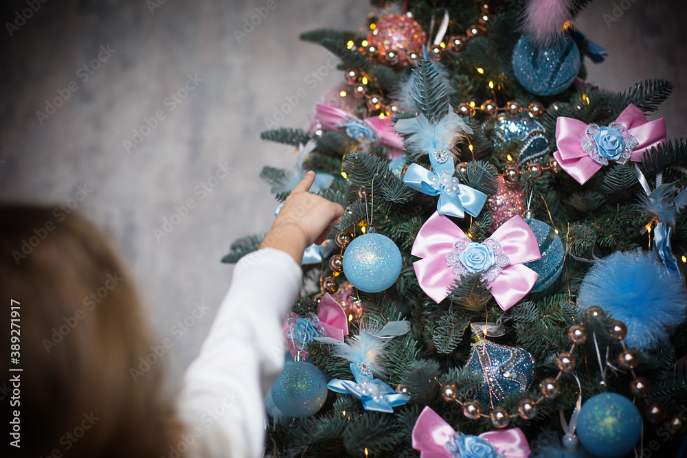 A little girl reaches for a Christmas tree toy with her hand. Christmas decor, waiting for a holiday and a miracle. New Year. White, pink and blue decor, Golden lights garlands A little girl reaches for a Christmas tree toy with her hand. Christmas decor, waiting for a holiday and a miracle. New Year. White, pink and blue decor, Golden lights garlands