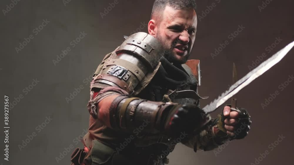 Brutal mature stalker with beard and blood on his face pulls his knives and screams then gets into fight stance with knives in dark background. Brutal mature stalker with beard and blood on his face pulls his knives and screams then gets into fight stance with knives in dark background.