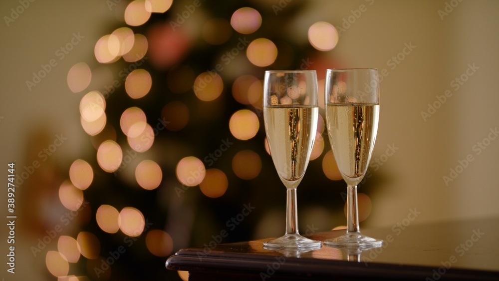 Two Bubbling Champagne Glasses Against The Backdrop Of Festive Decorations, Lights And Christmas Tree Defocused Background. Glasses with Sparkling Wine Holiday New Year Atmosphere