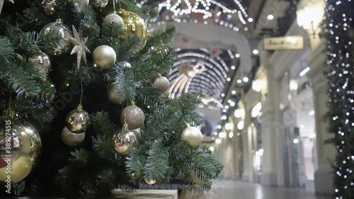 A Christmas tree decorated with Golden balls stands in the lobby of the shopping center against the background of shop windows.
