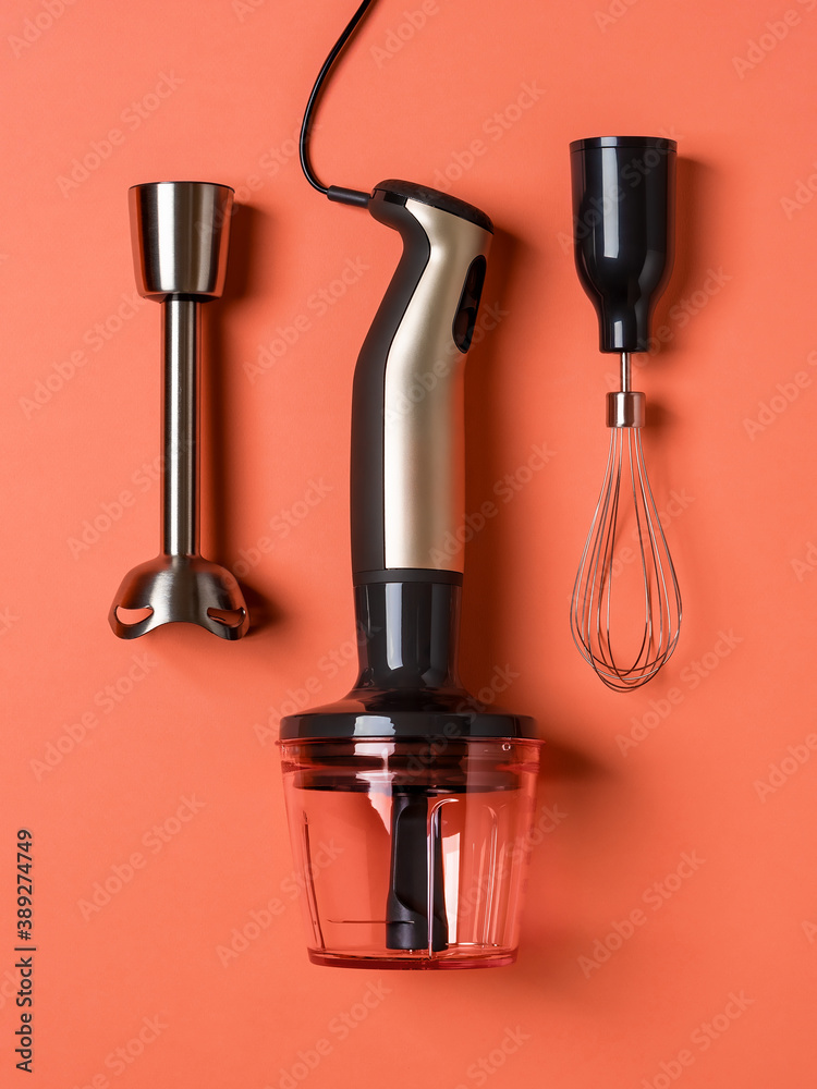 Immersion hand blender, whisk for whipping and chopper cup on a coral background. Modern electric kitchen appliances for making sauces, smoothies, puree. Hand mixer set. Immersion hand blender, whisk for whipping and chopper cup on a coral background. Modern electric kitchen appliances for making sauces, smoothies, puree. Hand mixer set.