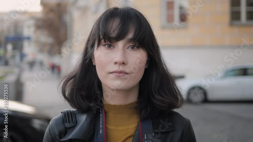 Young asian woman black hair closeup looking at the camera, background of city street. Handheld shot of beautiful asian girl in the street during windy weather