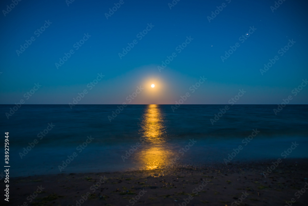 Fototapeta premium Landscape moon over horizon on sea and moonlight. Panorama with the luna of night. Lunar path on the water. Long exposure
