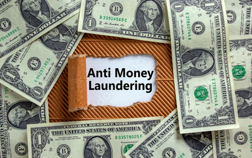 Anti Money Laundering concept. The text 'Anti Money Laundering' appearing behind torn brown paper. Dollar bills.
