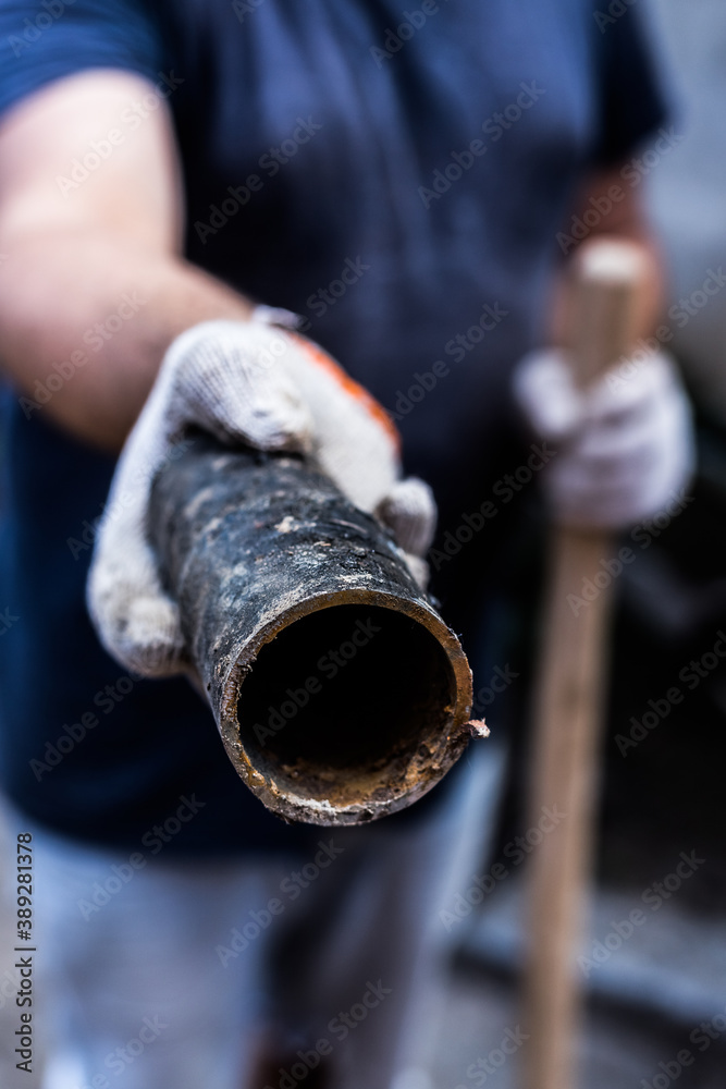 A worker holds in his hands piece of a metal pipe cut off